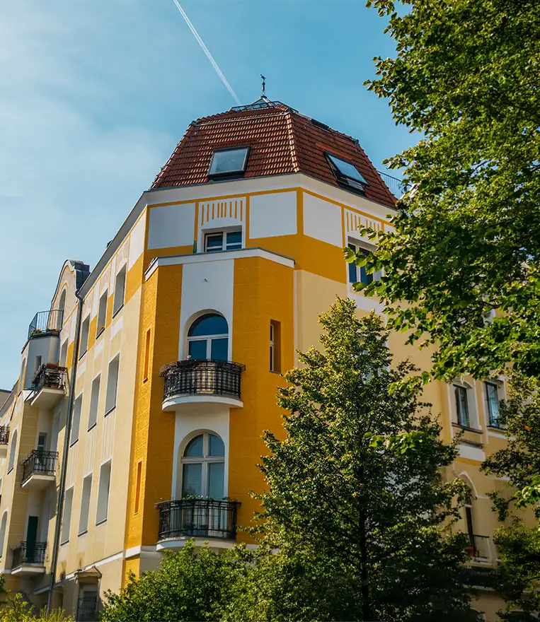 Saniertes gelbes Stadthaus im Altbau-Stil an einer Straßenecke.